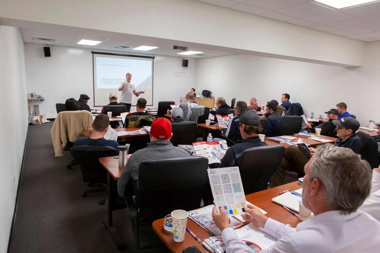Classroom session in progress: attendees at tables reviewing Polymer Nation system and color literature while an instructor presents